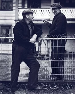 Two mature men talking over fence (B&W)