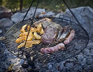 Meat and sausages being cooked on a grill hanging on chains