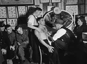 Prints of 8th November 1941: Leading tattooist Professor Cecil Rhodes of Dover completes a two-hour job on Seaman Collins, whose shipmate grips him by the shoulders for support Discover the Vision of Haywood Magee – A Master of Mid-Century British Life: Military Tattoo