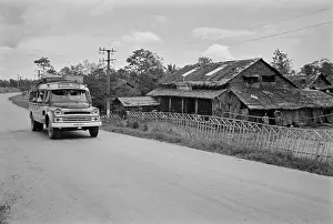 Prints of A minibus travels along a road, passing telegraph poles and a wood-built building, in Saigon, Vietnam, 30th August 1965 Vietnam Prints: Minibus, Saigon