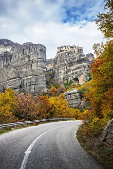 Monastery perched on a cliff, a road and autumn foliage