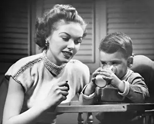 Mother assisting son (2-3) drinking milk, (B&W)