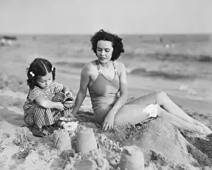Mother with girl (2-3) playing in sand on beach, (B&W)