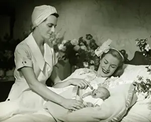 Helping Prints: Mother lying in bed smiling to baby-child (0-6 months), nurse standing beside, (B&W)