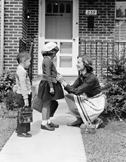 Mother outside front door, buttoning sweater of daughter going off to school with her brother