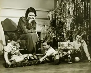 Enjoyment Prints: Mother watching three children playing by Christmas tree, (B&W)
