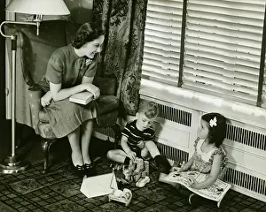 Quality Time Prints: Mother watching over son and daughter (4-5) playing in living room, (B&W)
