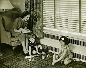 Mother watching over son and daughter (4-5) playing in living room, (B&W)