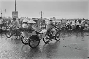Prints of A motorcycle rickshaw rider, wearing a safari-style hat, carrying passengers wearing traditional Vietnamese non la hats Vietnam Prints: Motorcycle Rickshaw, Saigon