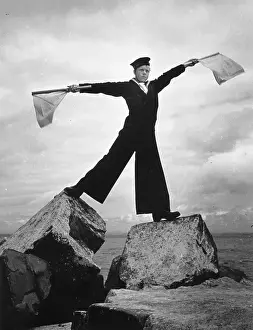Prints of 4th July 1942: A boy in Navy uniform standing on rocks to signal with semaphore flags. Original Publication: Picture Post - 1175 - The Basis Of British Sea Power - pub Discover the Vision of Haywood Magee – A Master of Mid-Century British Life: Naval Signals