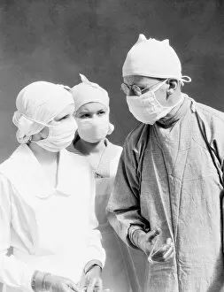 Two nurses and one doctor wearing surgical masks and gowns, looking at one another