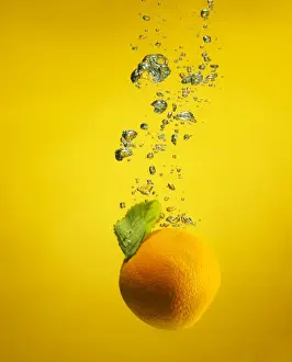 Prints of An orange splashed into water, creating bubbles, on yellow backdrop Stone Prints: An orange splashed into water