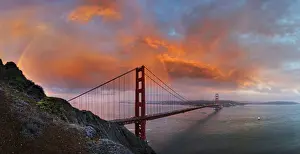 Cloudy Sky Prints: Panoramic view of the Golden Gate Bridge with a rainbow at sunset and orange-glowing storm clouds