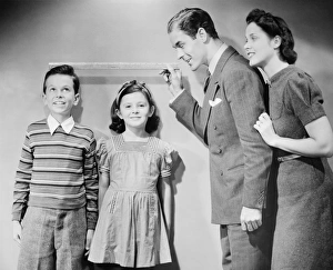 35 39 Years Collection: Parents measuring children standing against wall, boy (8-9) girl (6-7), (B&W)