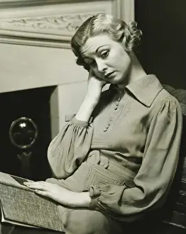 Introspection Prints: Pensive woman sitting by fireplace with book on laps, (B&W)