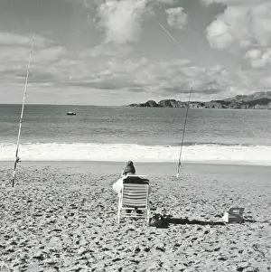 One Person Only Prints: Person sitting on beach with fishing poles embedded in sand and using cell phone