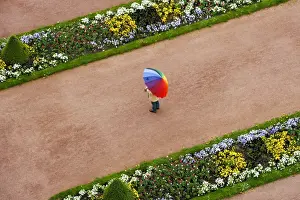 Public Park Prints: Person with umbrella in rainbow colors on a red gravel path between flower beds in the castle gardens