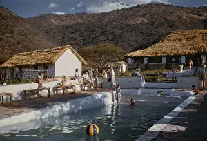 Prints of People relaxing at the poolside, with thatched buildings in the background, East Africa, circa 1955. (Photo by Raymond Kleboe/Picture Post/Hulton Archive/Getty Images) Moments of Everyday Brilliance: Poolside Relaxation, East Africa