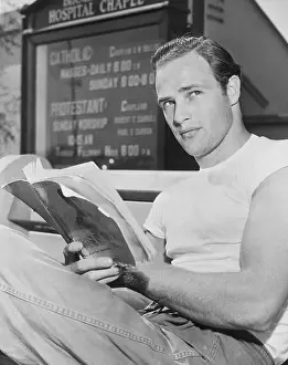 Prints of Marlon Brando is pictured sitting down reading a book outside the Hospital Chapel The Iconic Moments Captured: Portrait of Marlon Brando