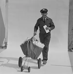 Postal worker carrying letters on wheel barrow against white background, portrait