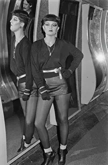 Prints of A young woman standing beside a curved mirror, wearing a black top with a headband, black gloves and a black leather miniskirt, location unspecified, March 1980 Fashion Trends Through Time Prints: Punk Fashions, 1980