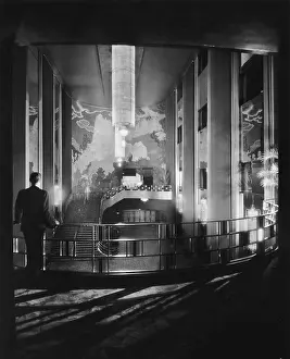 Prints of A man, seen from behind, leans against the railing of the gallery in the lobby of Radio City Music Hall in New York City Where New York’s brightest moments take center stage: Radio City