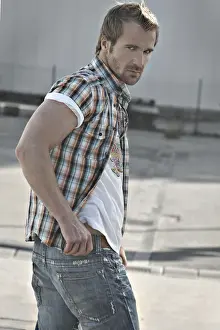 30 34 Years Prints: Rebellious man wearing jeans and a plaid shirt at a gas station, turning round