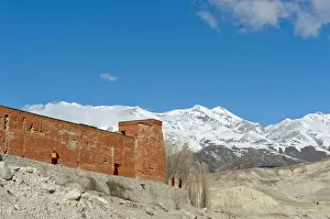 Red wall of a building with monks, Choede Gompa monastery, snow-capped mountains of Mustang Himal mountain range at