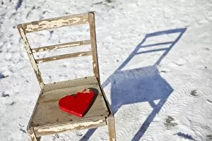 Red wooden heart placed on an old chair in snow