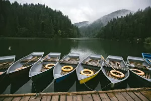 Rowing boats moored at the pier near mountain lake surrounded by misty forest