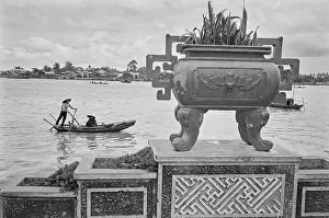 Prints of An ornamental planter and a sampan, with passengers wearing traditional Vietnamese non la hats, on the waters of the Saigon River as it flows through Saigon, Vietnam, 30th August 1965 Vietnam Prints: Saigon River, Vietnam