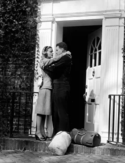 Dedication Gallery: Sailor with duffel bags, hugging woman, about to kiss on front doorstep