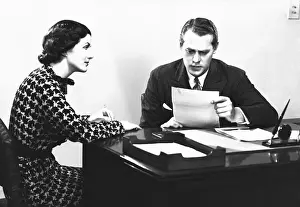 Secretary assisting businessman reading document at desk, (B&W)