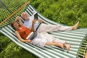 Shop Gallery: Senior citizen couple lying in a hammock, woman wearing a headset looking at a netbook or laptop