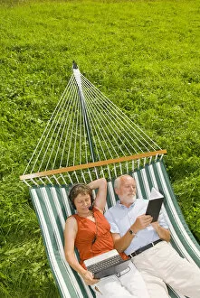 Satisfaction Gallery: Senior citizen couple, woman wearing a headset looking at a netbook or laptop, man reading a book