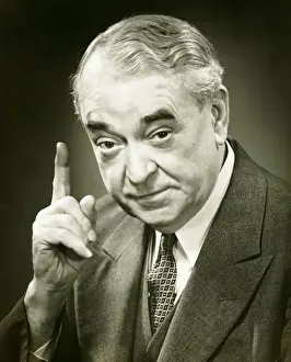 Senior man raising index finger in studio, (B&W), close-up, portrait