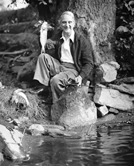 Senior Men Prints: Senior man sitting by water, holding up fish (B&W), portrait
