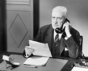 Worried Prints: Senior talking on phone at desk in office (B&W)