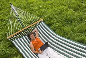 Senior Women Prints: Senior woman with netbook and headset lying in a hammock