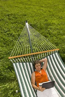 Senior Women Prints: Senior woman with netbook and headset lying in a hammock