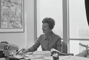 Prints of 1967, One Person, Adults Only, Senior Adult, One Woman Only, One Senior Woman Only, Caucasian Appearance, Indoors, Day, Horizontal, Black And White, Photography, Head And Shoulders, Smart Tom Kelley Archive Prints: Senior woman sitting at desk writing on notepad, smiling