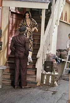 Prints of American actor Robert Redford wearing a striped brown suit and a grey newsboy cap (back to camera) talking to American actress Eileen Brennan, who wears a floral pattern bathrobe Robert Redford: Classic Hollywood Elegance: On The Set Of The Sting