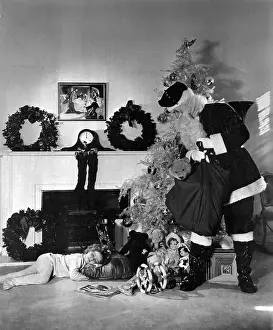 Prints of (Original Caption) 12/3/1934- Los Angeles, CA- The clock on the mantelpiece says twelve--long after good little girls should be in bed, and Shirley Temple, although not snug in her nursery A Timeless Christmas: Vintage Treasures: Shirley Temple Sleeps as Santa Delievers