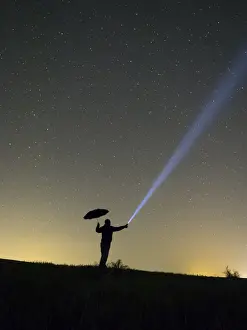 Risk Prints: Silhouette of a man at night, in the rain, making signals with a flashlight
