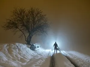 Warm Clothing Prints: Silhouette of a person walking with a suitcase along a covered way of snow and fog during the night