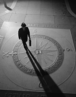 Silhouetted businessman with briefcase walking across compass in the sidewalk