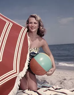 Facial Expression Gallery: Smiling Blonde Woman Bathing Suit Hold Beach Ball Kneel In Sand By Red Sun Umbrella