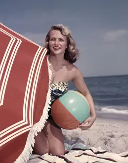 Suit Prints: Smiling Blonde Woman Bathing Suit Hold Beach Ball Kneel In Sand By Red Sun Umbrella