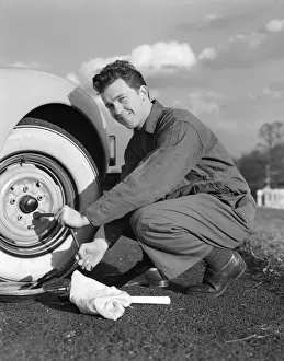 Smiling man in coveralls using tire iron to change tire on sedan