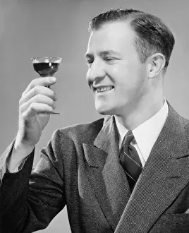 One Mid Adult Man Only Prints: Smiling man holding up short glass with drink, (B&W), close-up